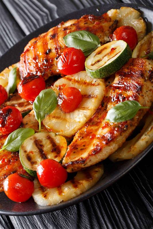 Chicken fillet grilled with pineapple, zucchini and tomatoes in a spicy sauce close-up on a plate. vertical , stock photo