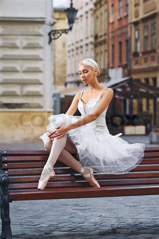 Vertical portrait of a graceful ballerina sitting alone on the bench in the city street grace elegance femininity sensuality loneliness art, stock photo
