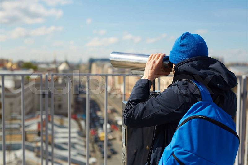 Back view portrait of contemporary tourist looking over city from viewing platform on the roof, using coin operated binoculars, stock photo