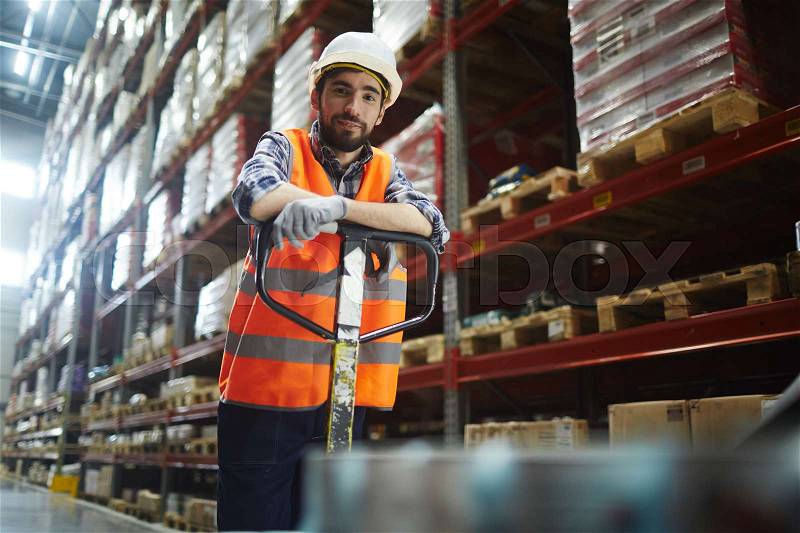 Portrait of cheerful warehouse loader at work, pushing moving cart and looking at camera, stock photo
