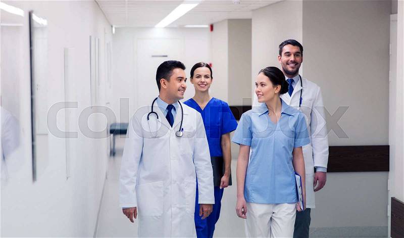 Clinic, profession, people, healthcare and medicine concept - group of happy medics or doctors walking along hospital corridor, stock photo