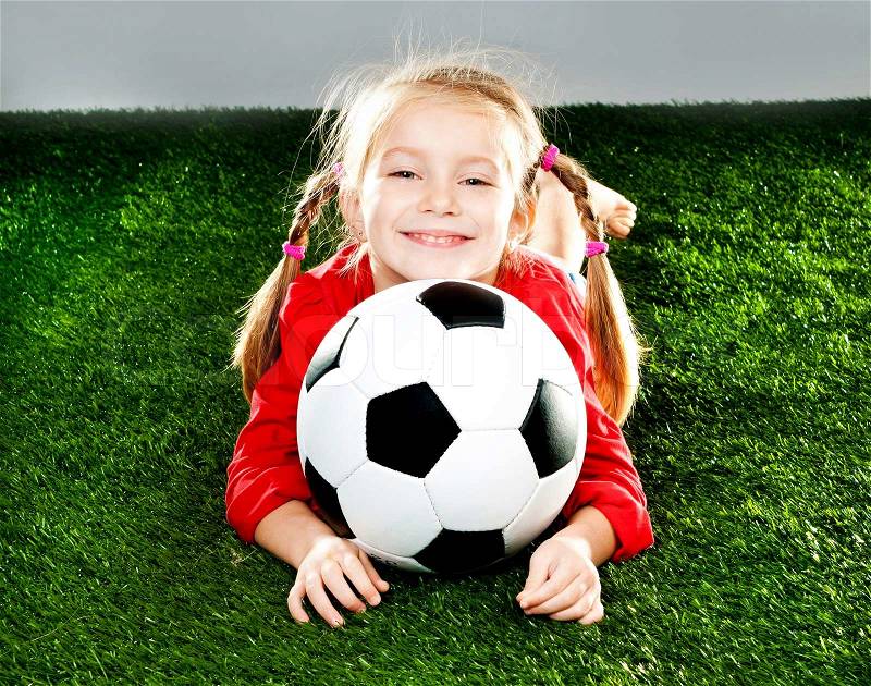 Little girl with soccer ball in boots on a green lawn, stock photo