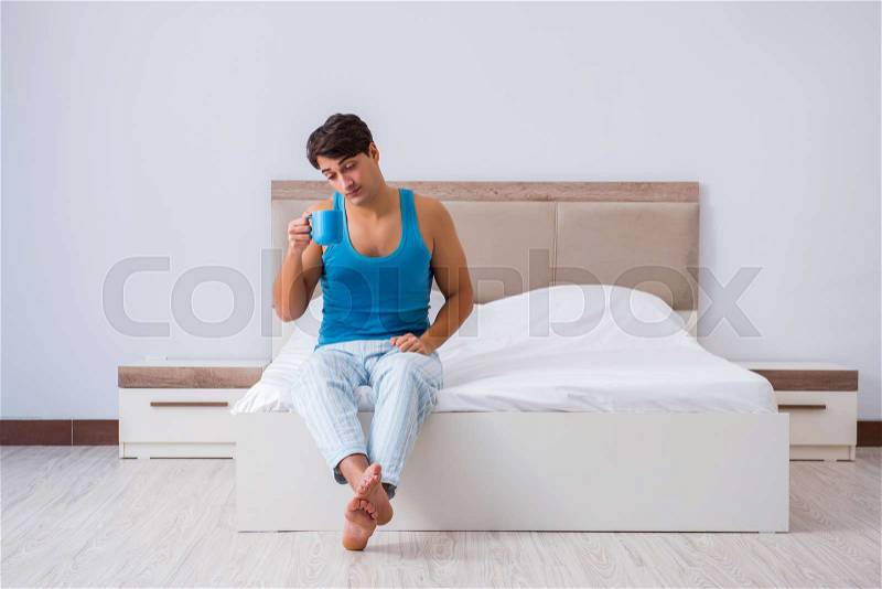 Young man waking up in bed, stock photo