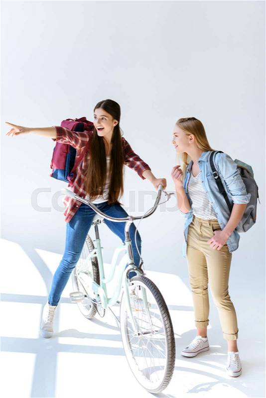 Smiling teenage girl pointing away with friend standing near by isolated on white, stock photo