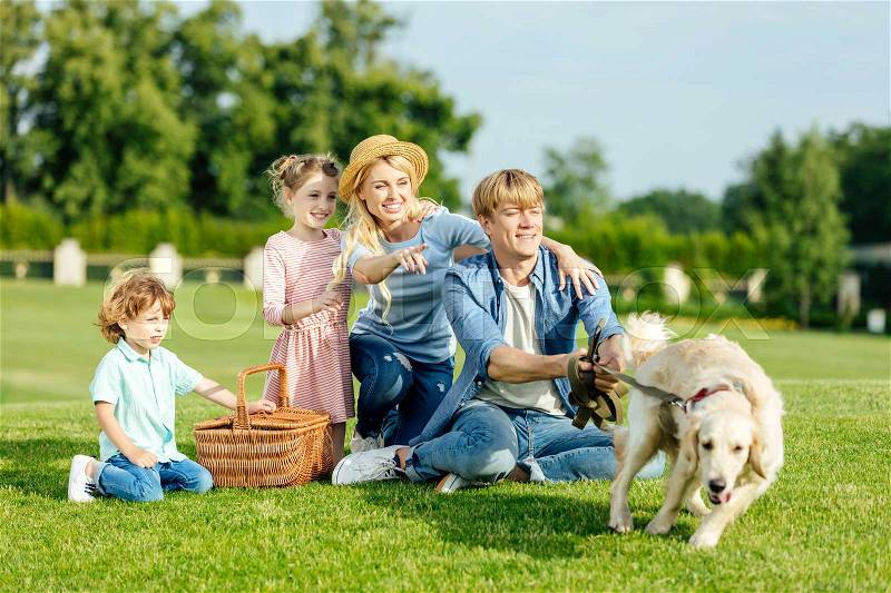 Happy young family with dog resting on green grass at picnic , stock photo
