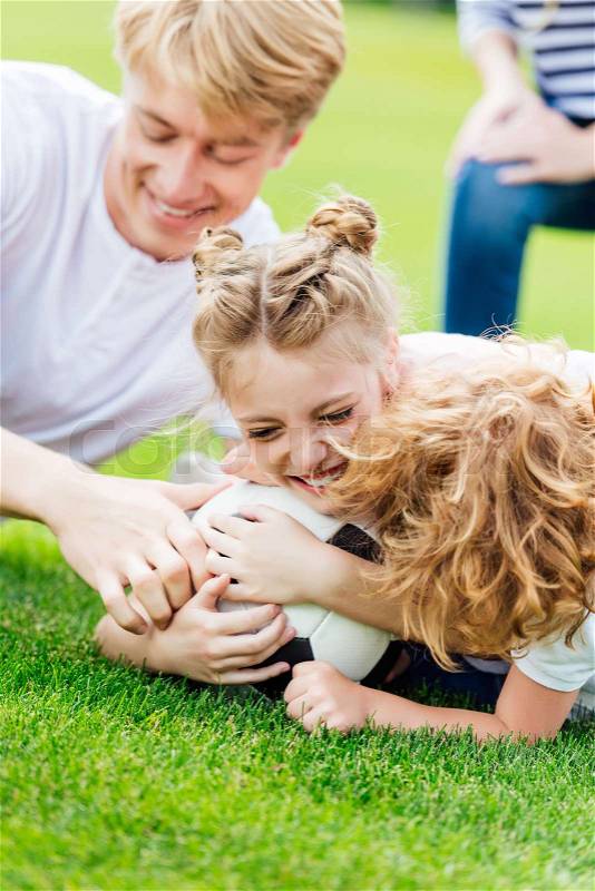 Happy father with cute little children playing soccer on green lawn, stock photo