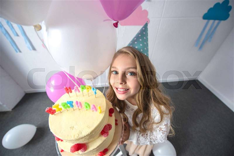 Cheerful little girl holding birthday cake and smiling at camera, stock photo