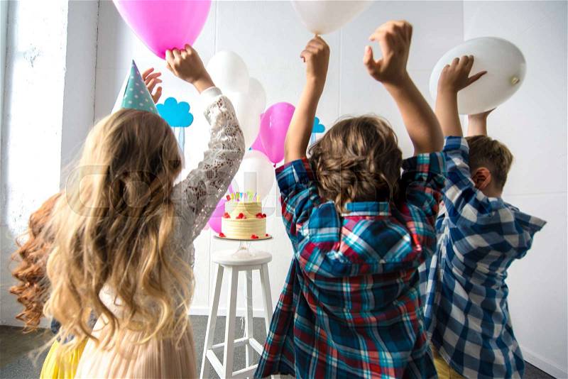 Back view of cute cheerful kids reaching to birthday cake, stock photo