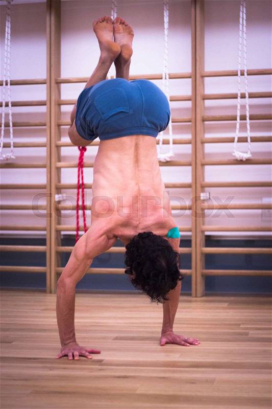 Male yoga teacher doing handstand inversion alisthenics and yoga asana practice in gym fitness pilates studio, stock photo