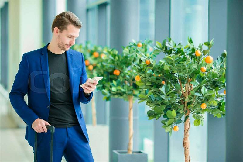 Urban businessman talking on smart phone inside in airport. Casual young boy wearing suit jacket. Caucasian man with cellphone at the airport while waiting for boarding, stock photo