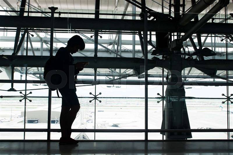 Waiting in the airport, using smartphone, silhouette backpacker using technology, stock photo