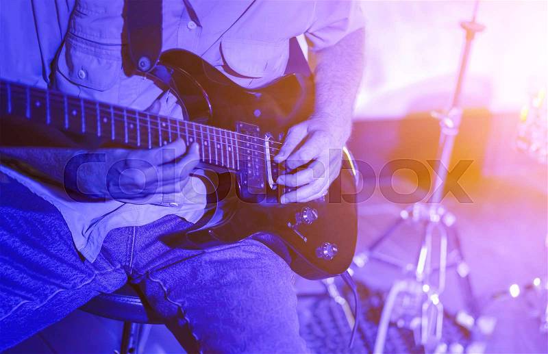 Man playing the guitar on stage closeup illuminated in blue light, stock photo
