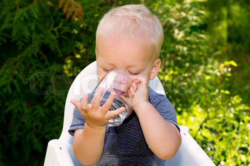 Funny wet baby boy trying to drink water from the glass independently, stock photo