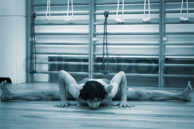 Male yoga teacher doing splits calisthenics and yoga asana practice in gym fitness pilates studio, stock photo