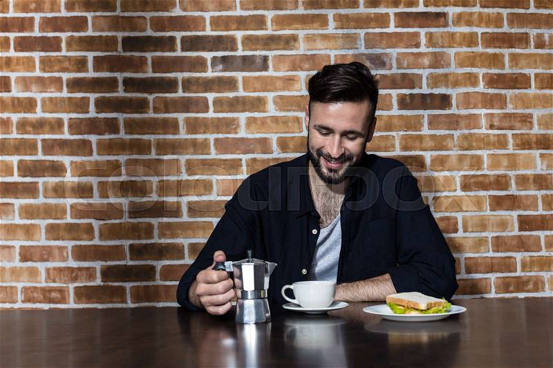 Handsome bearded young man drinking coffee and eating sandwich at morning, stock photo