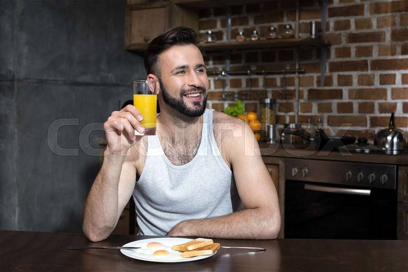 Handsome bearded young man drinking juice while eating breakfast at home, stock photo
