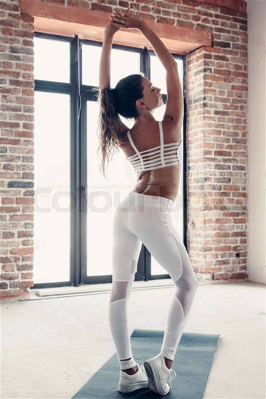 Young beautiful girl wearing fashion sports wear doing exercise on mat at loft gym, stock photo