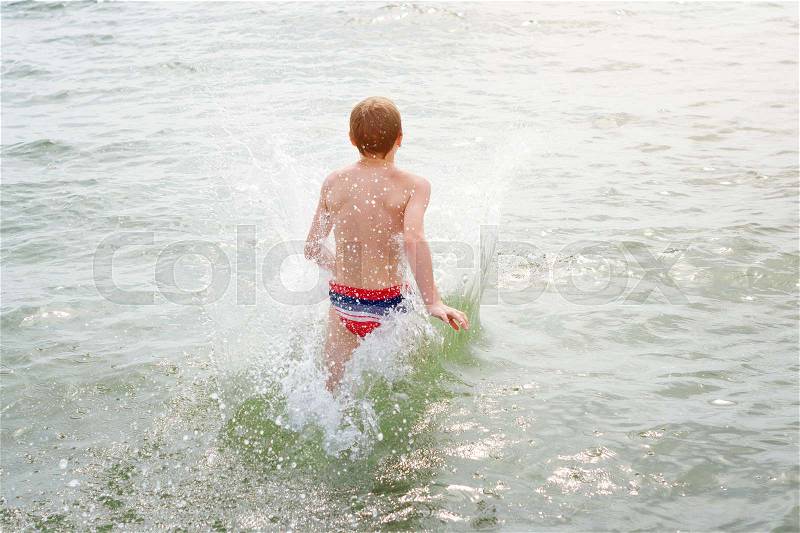 Boy jumping in sea waves. Jump with water splashes. Summer vacation, sunny day, ocean coast. Toned image, stock photo