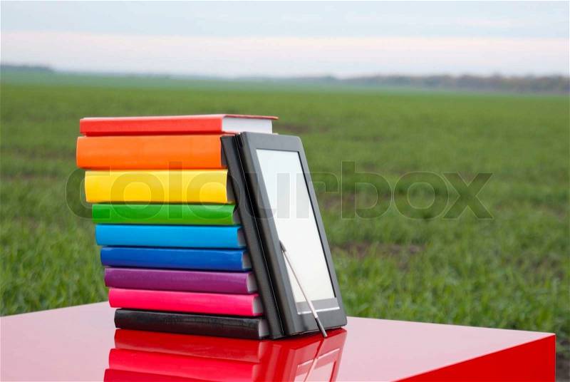 Stack of colorful books and electronic book reader outdoors, stock photo