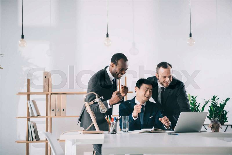 Funny team of multiethic businessmen looking at laptop screen, stock photo