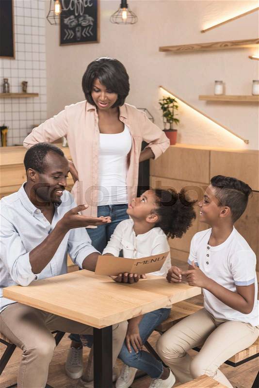 Funny african-american family looking at menu list in cafe, stock photo