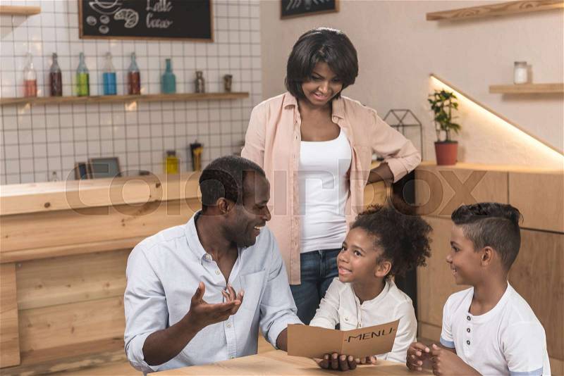 Cute african-american family looking at menu list in cafe, stock photo