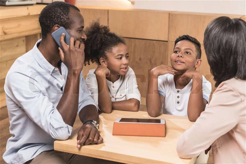 Cute african-american family sitting in cafe while father talking by phone, stock photo