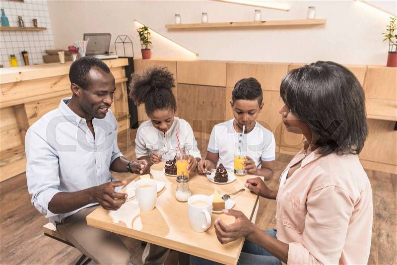 Beautiful african-american family eating desserts in cafe, stock photo