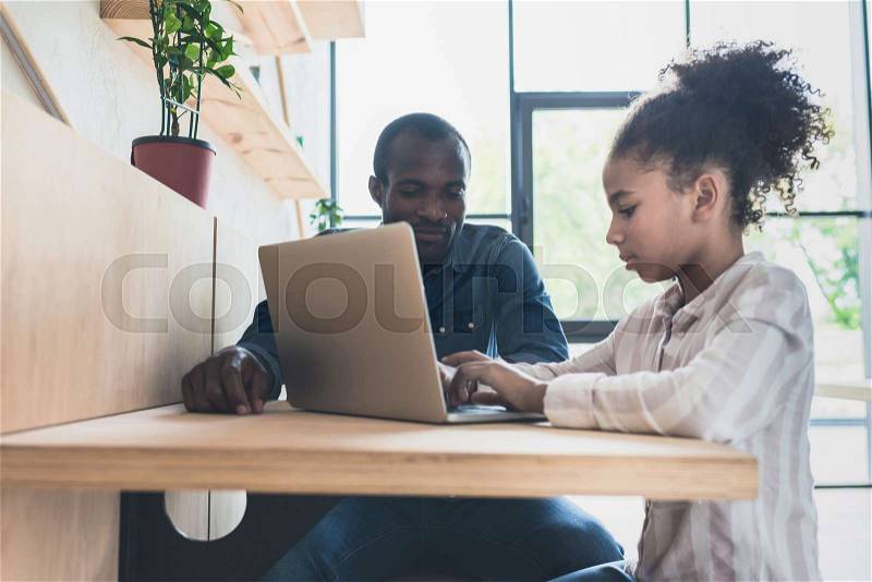 African-american father and daughter sitting in cafe with laptop, stock photo