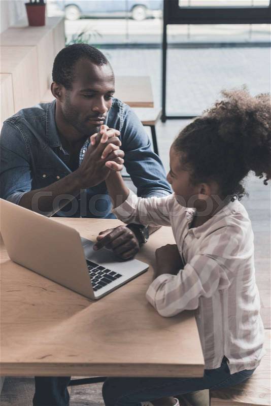 African-american father and adorable daughter sitting in cafe with laptop, stock photo