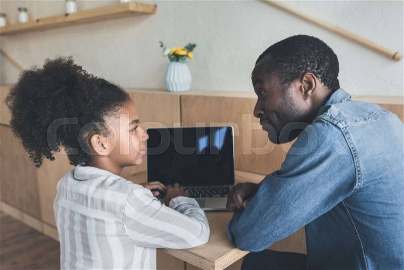 Beautiful african-american father and daughter sitting in cafe with laptop, stock photo