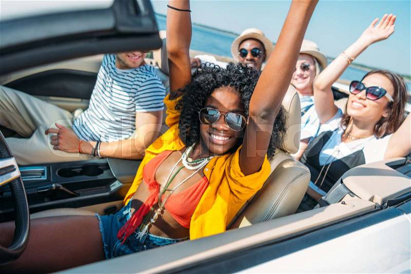 Multiethnic smiling friends riding car while traveling together, stock photo