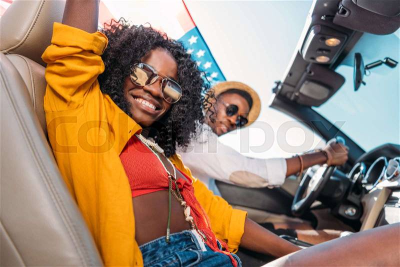 Side view of smiling african american couple with american flag riding car, stock photo