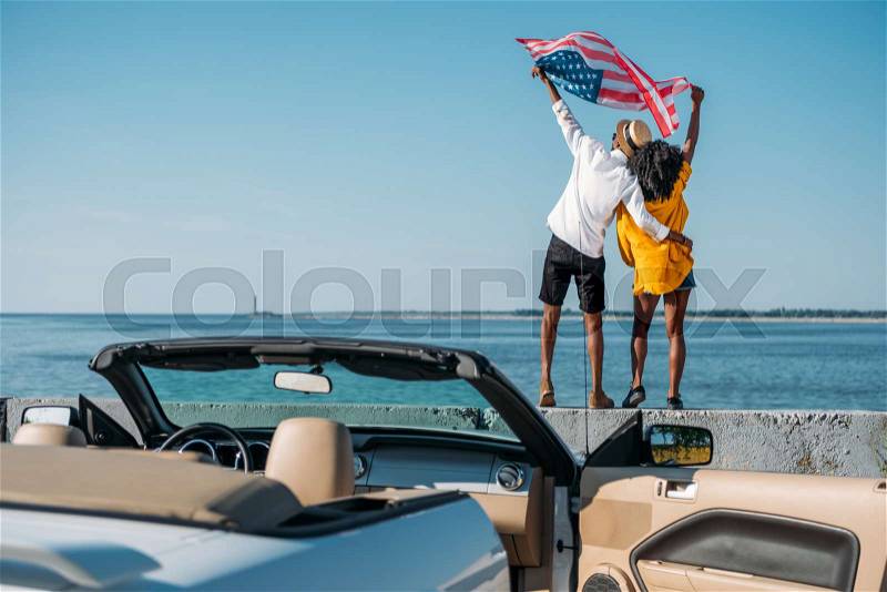 Back view of african american couple with american flag standing on parapet together, stock photo