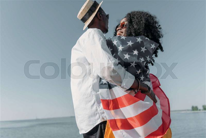 Side view of african american man hugging girlfriend in american flag, stock photo