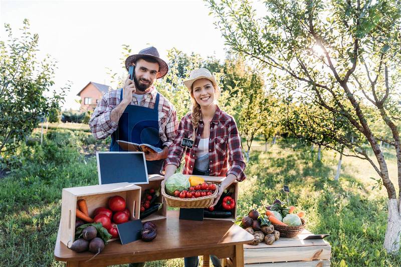 Two smiling farmers selling organic locally grown vegetables at market, stock photo