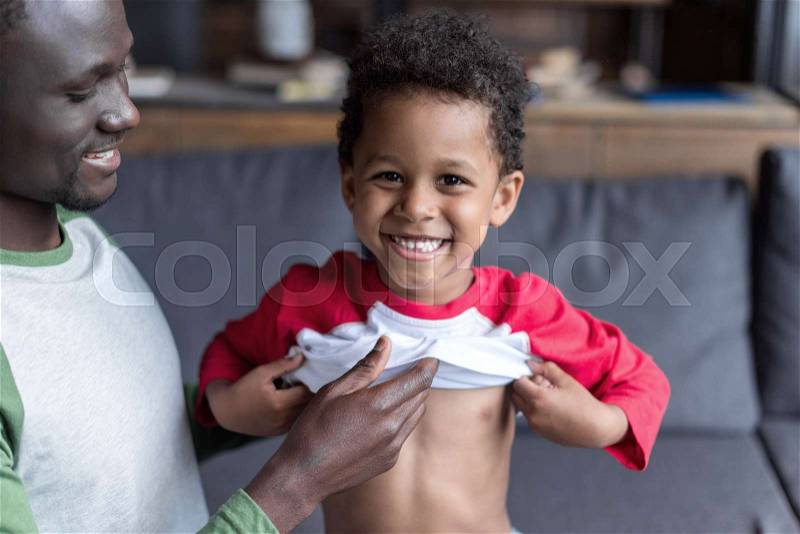 Close-up shot of loving african-american father dressing up his son, stock photo