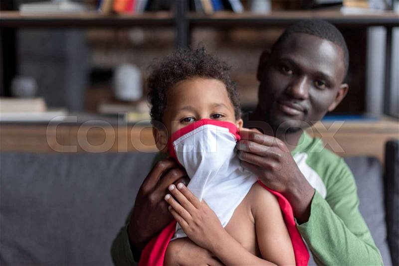 Close-up shot of loving african-american father dressing up his cute son, stock photo