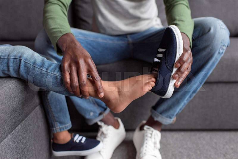 Cropped shot of african-american father putting shoes on son, stock photo
