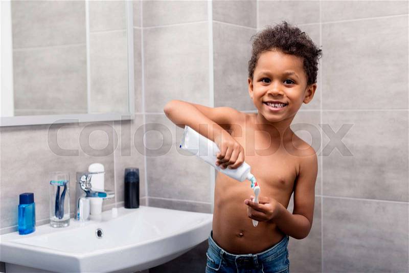 Adorable african-american kid applying tooth paste on brush, stock photo
