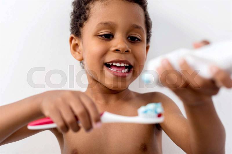 Adorable african-american kid applying tooth paste on brush, stock photo
