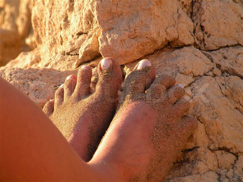 Sanded feet in the evening sun leaning against rocks, stock photo