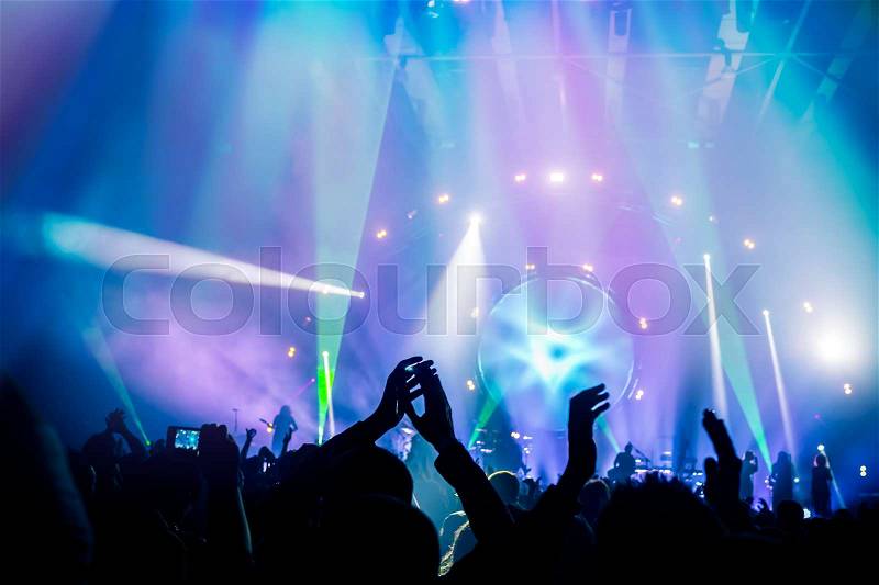 Many people enjoying concert, band performs on stage in the bright blue light, people enjoying music, dancing with raised up hands and clapping, active night life , stock photo