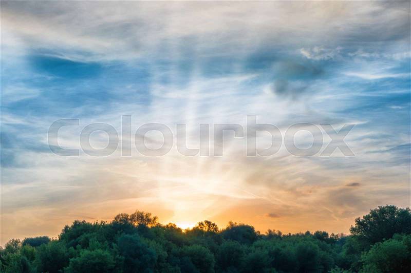 Sunset over forest silhouette. Dramatic sky with sun and clouds, stock photo