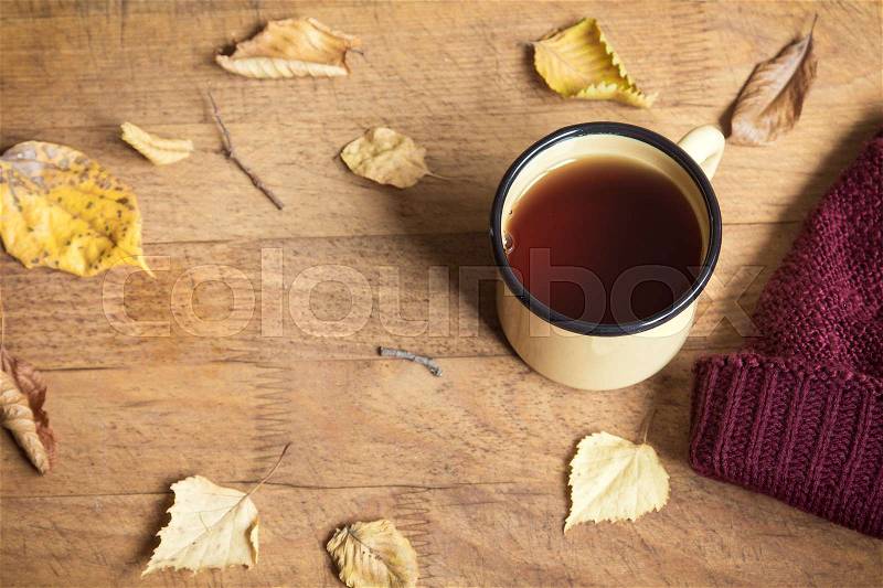 Hot autumn tea and yellow dry leaves, top view. Seasonal cozy drink in mug on wooden background with leaves. Hot drink for autumn cold days, stock photo