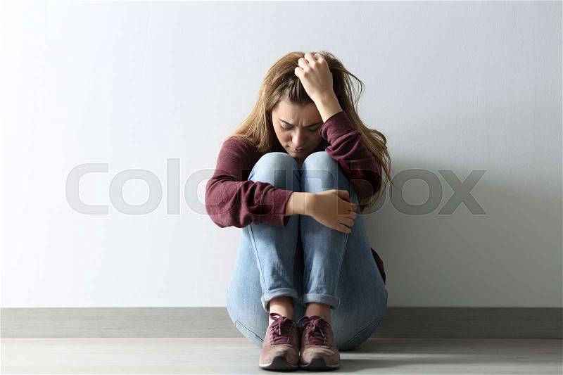 Front view full body portrait of a sad woman sitting on the floor at home, stock photo