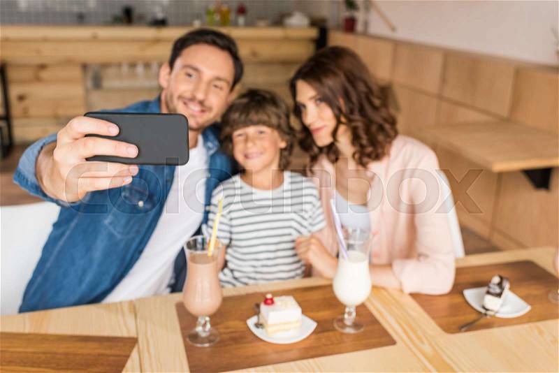 Young happy family taking selfie in cafe with desserts and milkshakes, stock photo