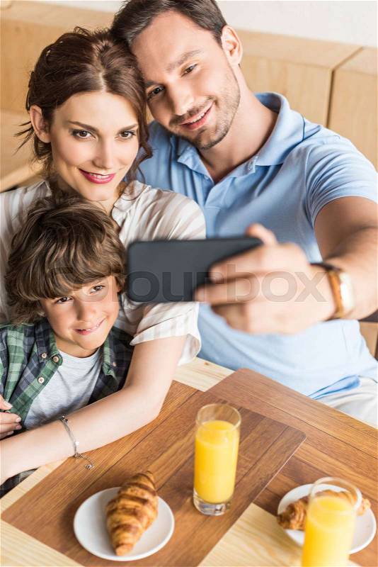 Young happy family taking selfie with smartphone in cafe, stock photo