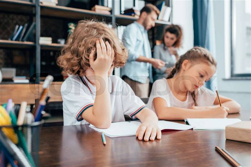 Exhausted little kids doing homework together, stock photo