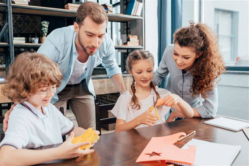 Happy young parents doing homework with kids, stock photo